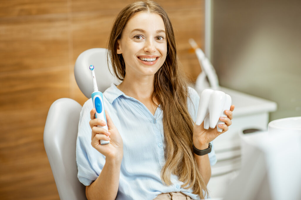 Young female patient holding an electric toothbrush while in dental chair, promoting modern dental hygiene practices.